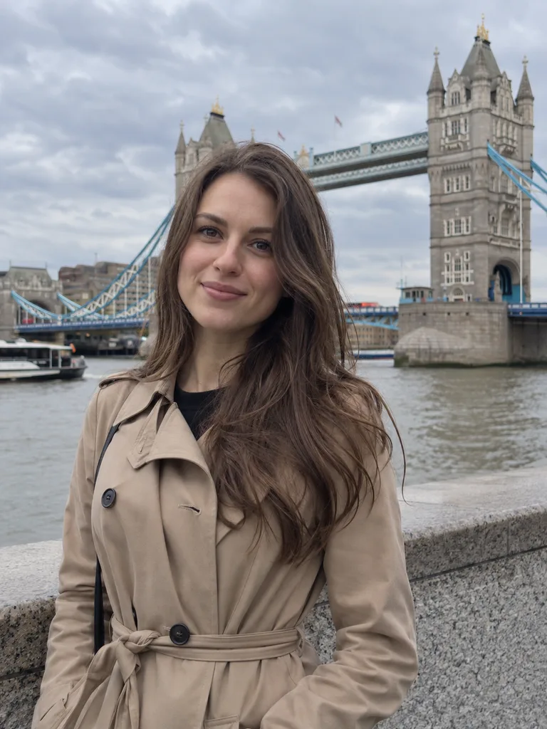 Une jeune femme aux longs cheveux bruns vêtue d'un trench-coat beige devant le Tower Bridge à Londres